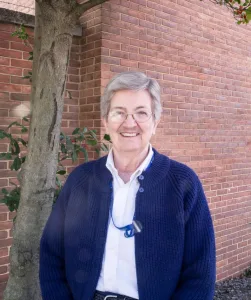 Photography portrait of Sister Mary Jean Doyle standing smiling outside of a building.
